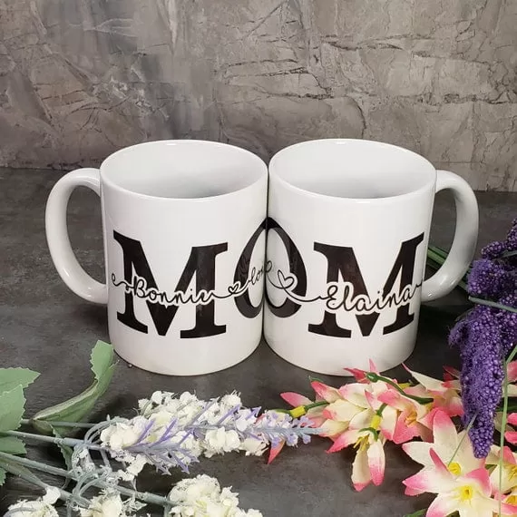 11 oz white porcelain coffee mug. Personalized with the word "mom" in large black font. In the center of the word "mom" are children's names in a black cursive font.