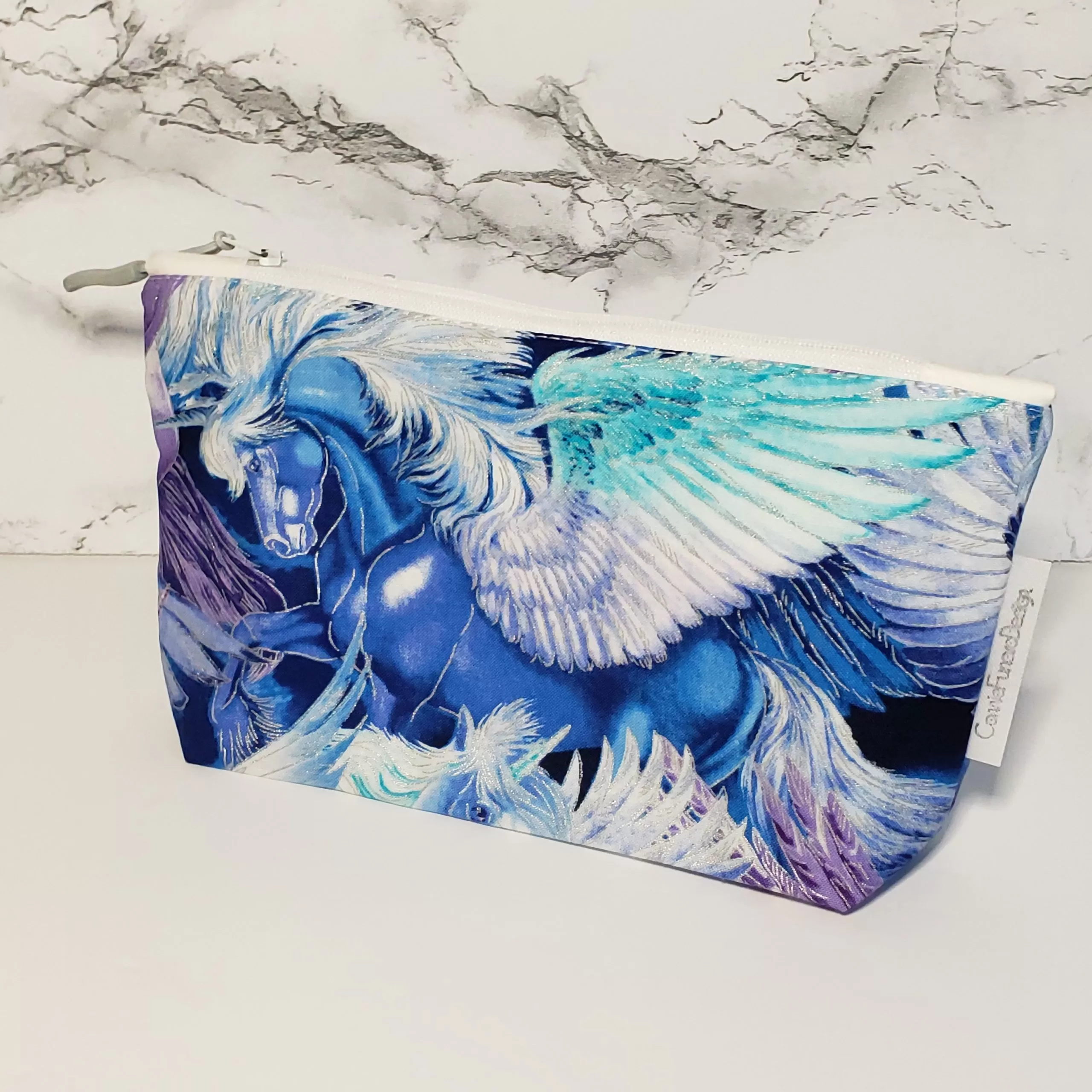 Flying horse mystical creature theme with metallic fabric accents. Structured box bottom accessory bag. Lined with white fabric and matching zipper. Convenient zipper pull. 100% Cotton fabric. Measures 8.5 inches wide, 5 inches tall.