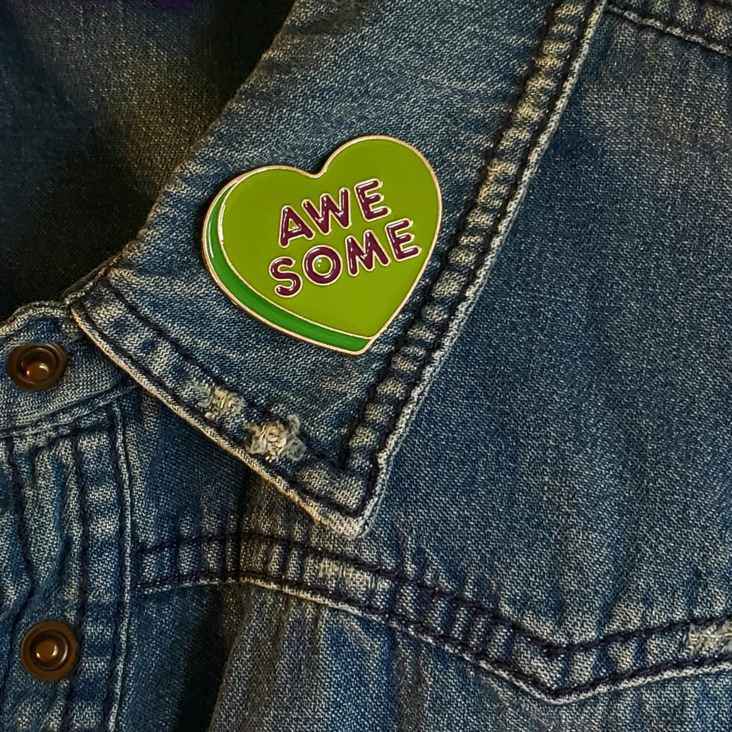 Green retro heart shaped enamel pin with the word AWESOME. Shown on a denim jacket