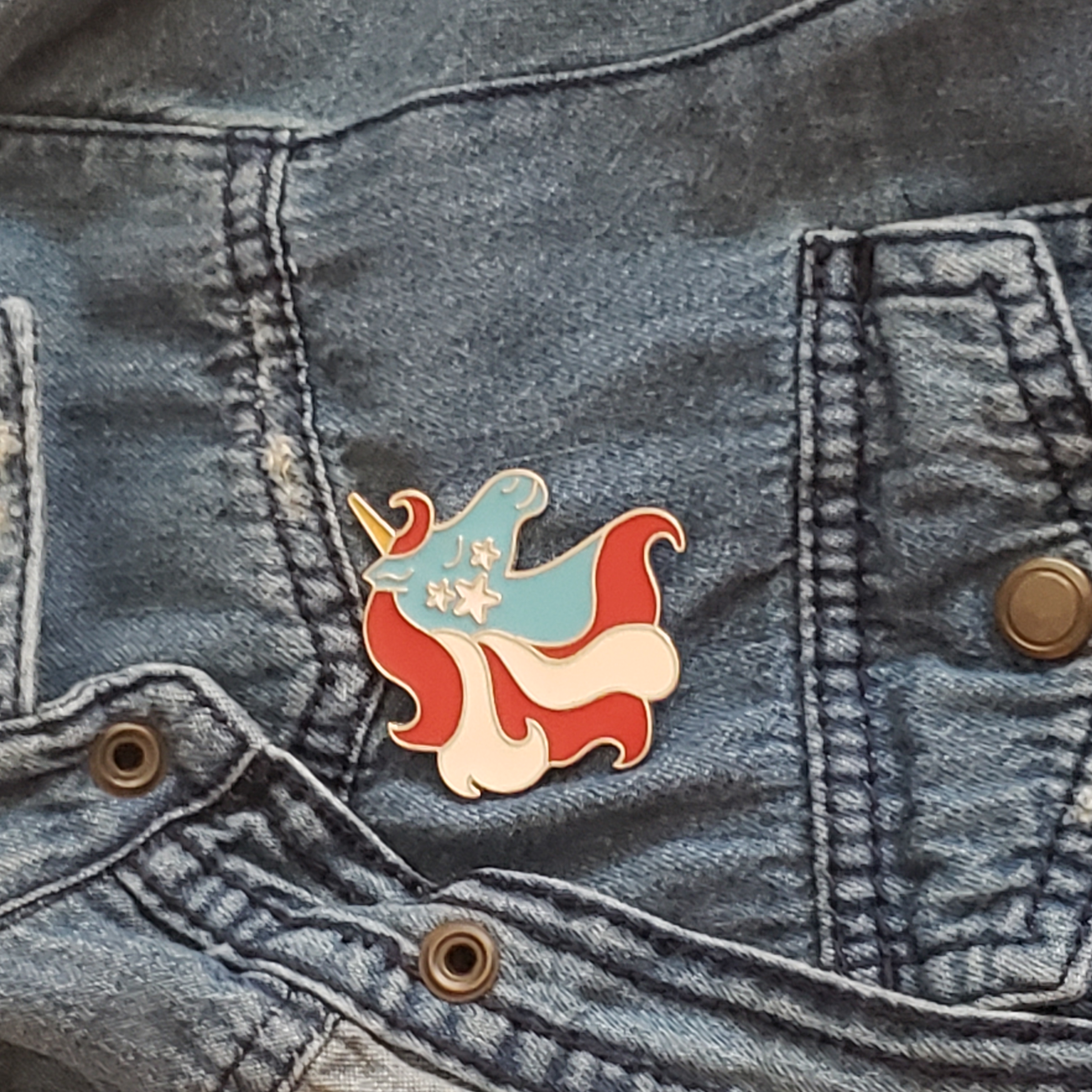 Large retro unicorn enamel pin. red, white and blue. Shown on denim jacket.