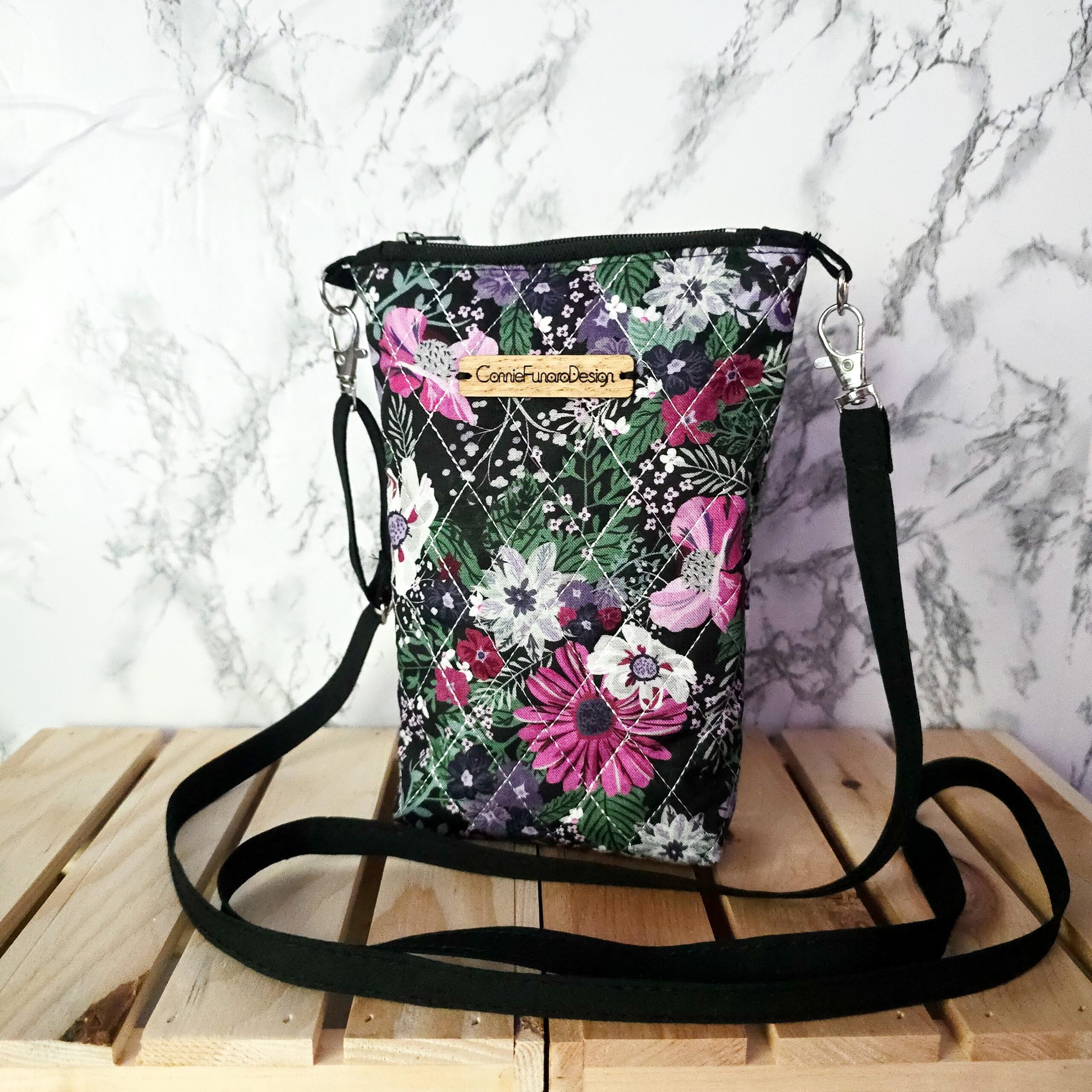Quilted wildflower design crossbody phone bag, 8 inches long and 5 inches wide, featuring a zip closure, coordinating liner, adjustable 50-inch strap, and metal hardware.
