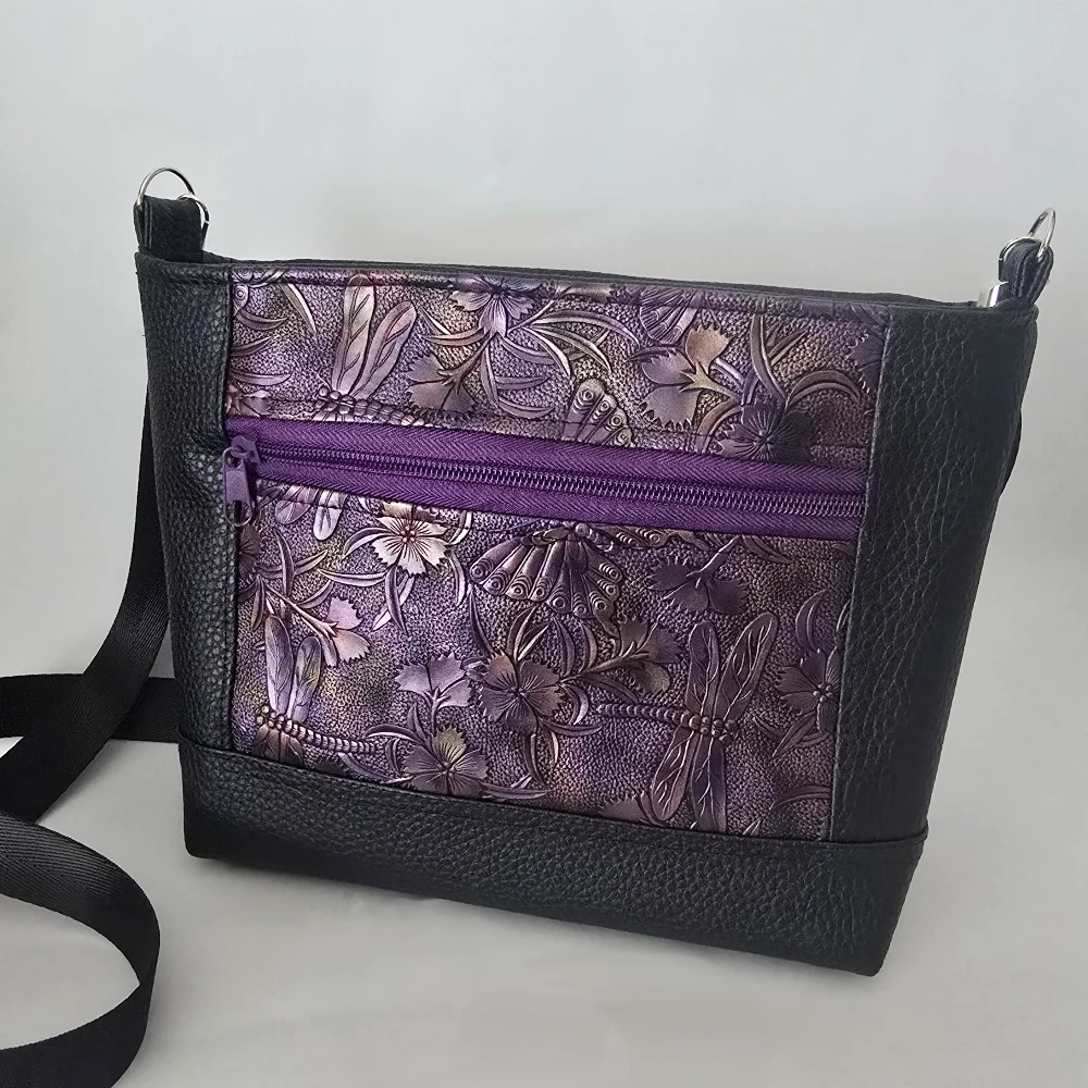Purple dragonfly embossed vegan leather purse with black trim and adjustable shoulder strap.