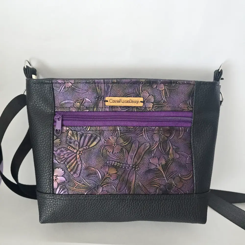 Purple dragonfly embossed vegan leather purse with black trim and adjustable shoulder strap.