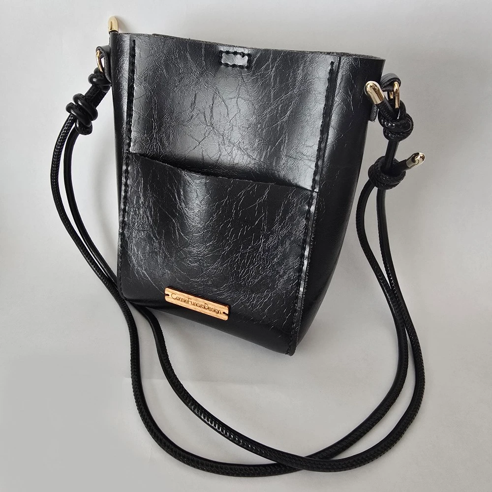 Handmade black bucket bag with vegan leather, gold-tone hardware, magnetic closure, front pocket, and adjustable strap. Compact and versatile for everyday use.